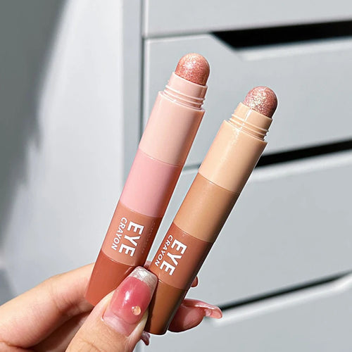 Hand holding two shimmery dual-ended eye crayon makeup sticks in pink and nude shades