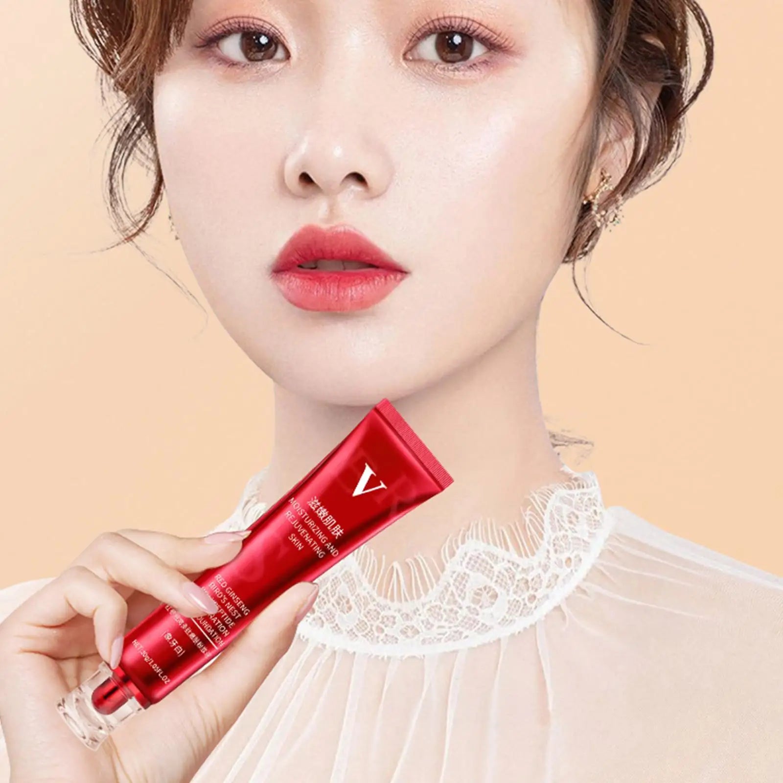 Woman with natural makeup holding red skincare cream tube in front of peach background