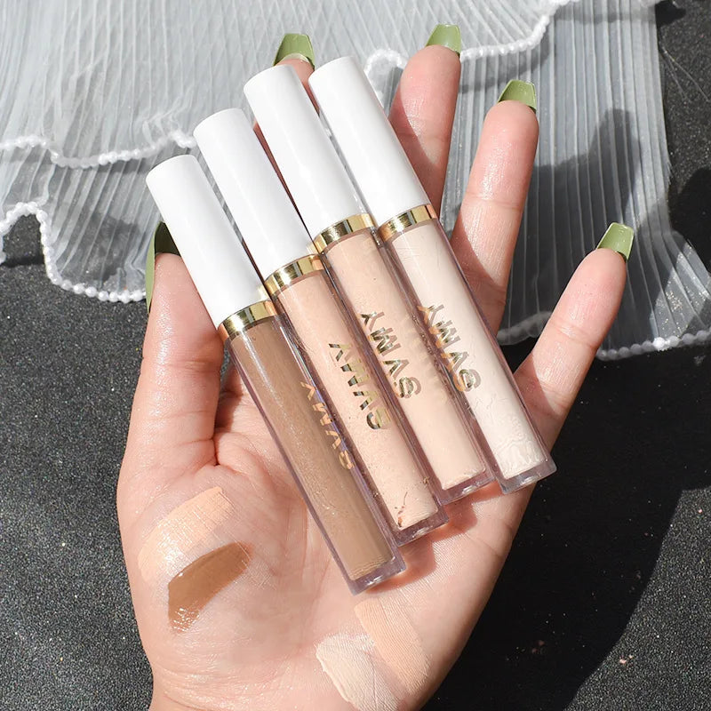 Hand holding four liquid concealers in neutral shades, swatched on skin, makeup product