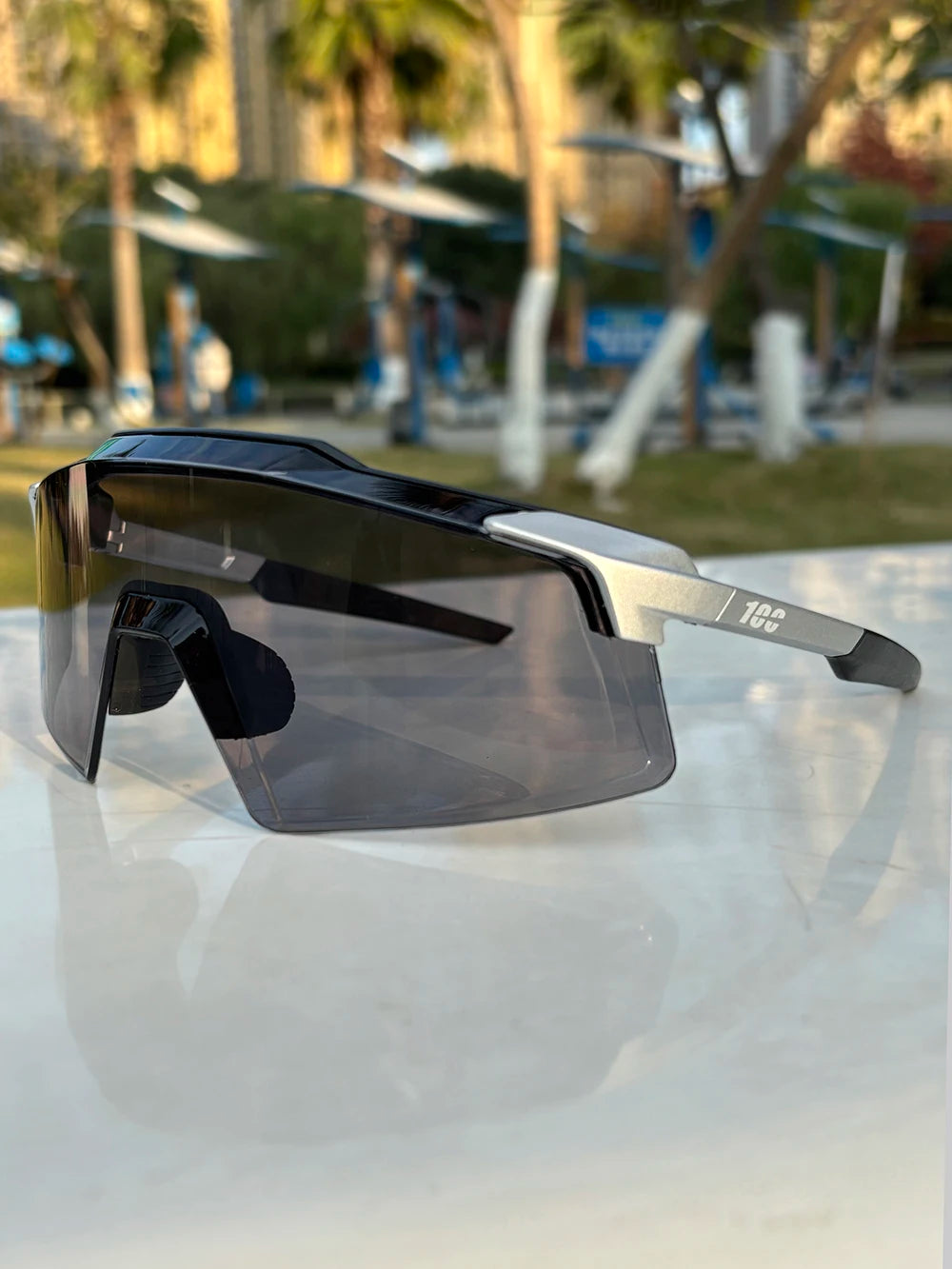 Sporty wraparound sunglasses with black tinted lenses and silver accents, outdoor setting