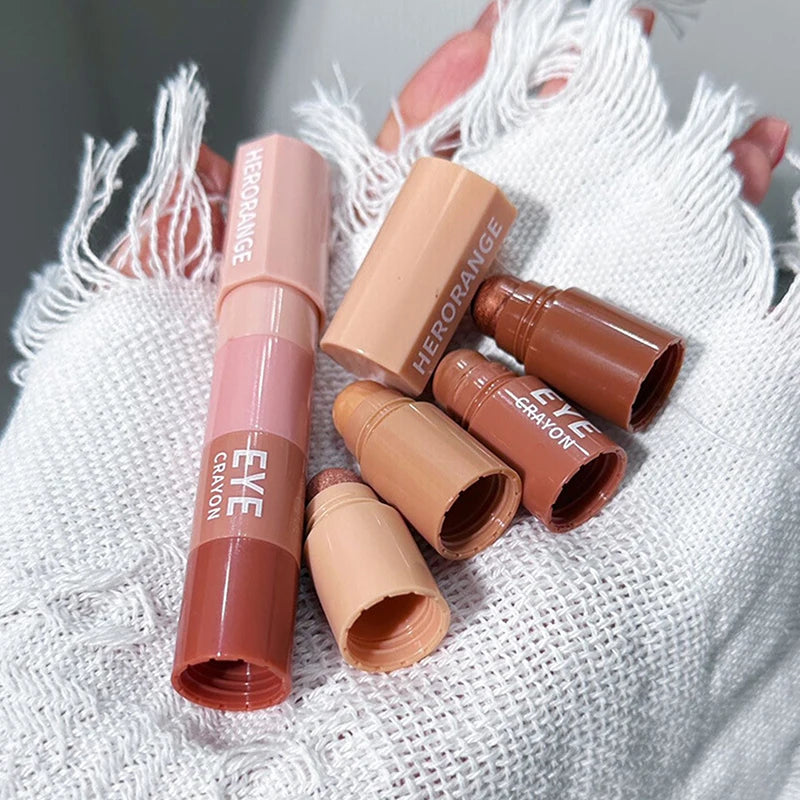 Set of nude and brown eye crayon makeup sticks on a textured white fabric background