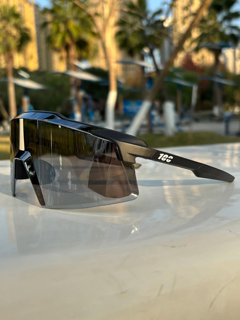 Black sporty sunglasses with reflective lenses on a white table outdoors, palm trees in background