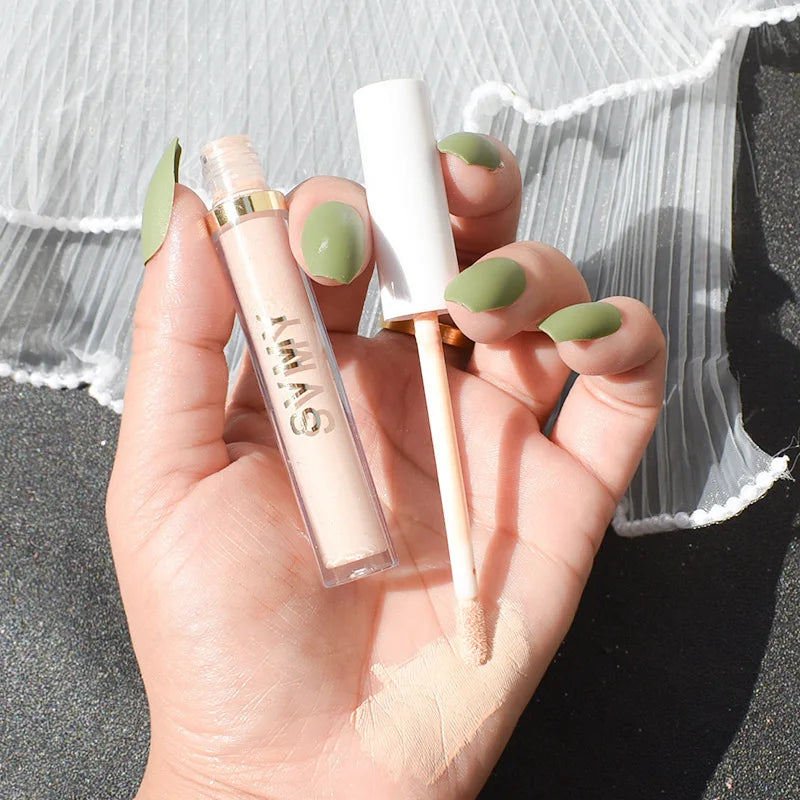 Hand holding liquid concealer tube with applicator and green manicured nails