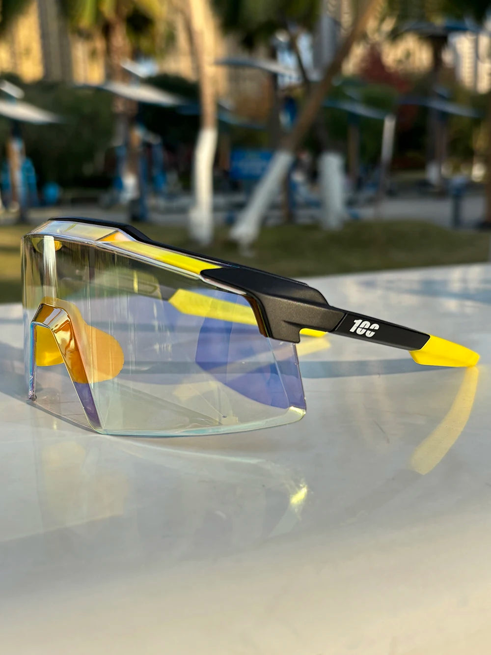 Futuristic yellow and black shield sunglasses with large mirrored lens on outdoor table