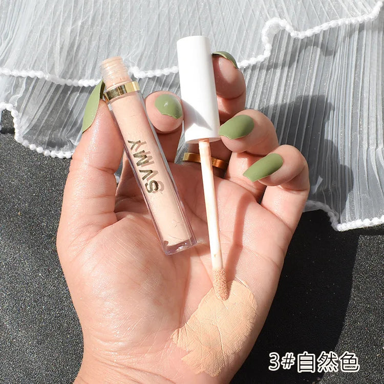 Hand holding SYNY liquid concealer with applicator, beige shade swatched on skin