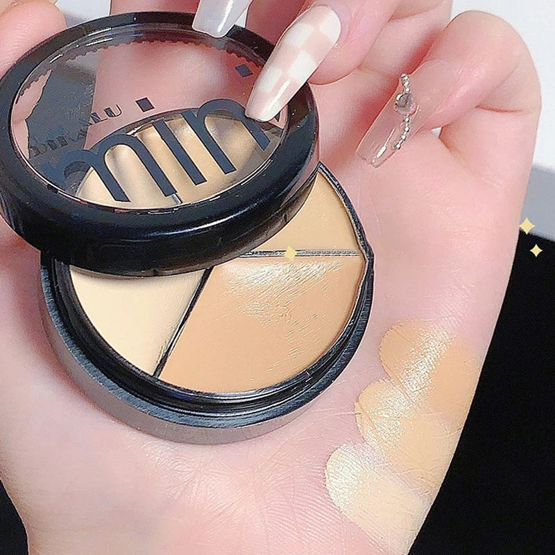 Hand holding a three-shade cream concealer palette with swatches on the skin