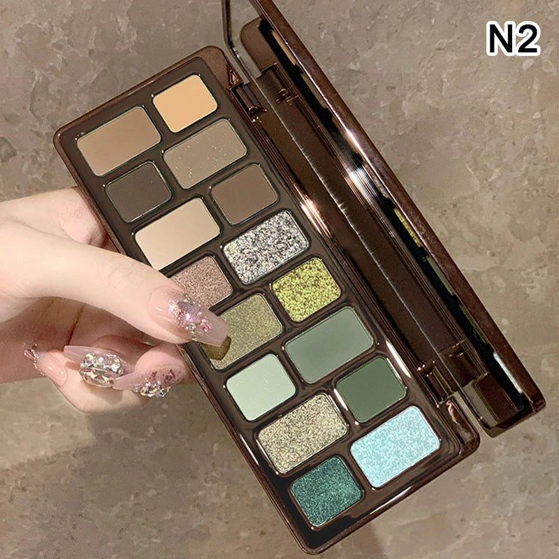 Hand holding eyeshadow palette with green, gold, brown, and glitter shades on neutral background